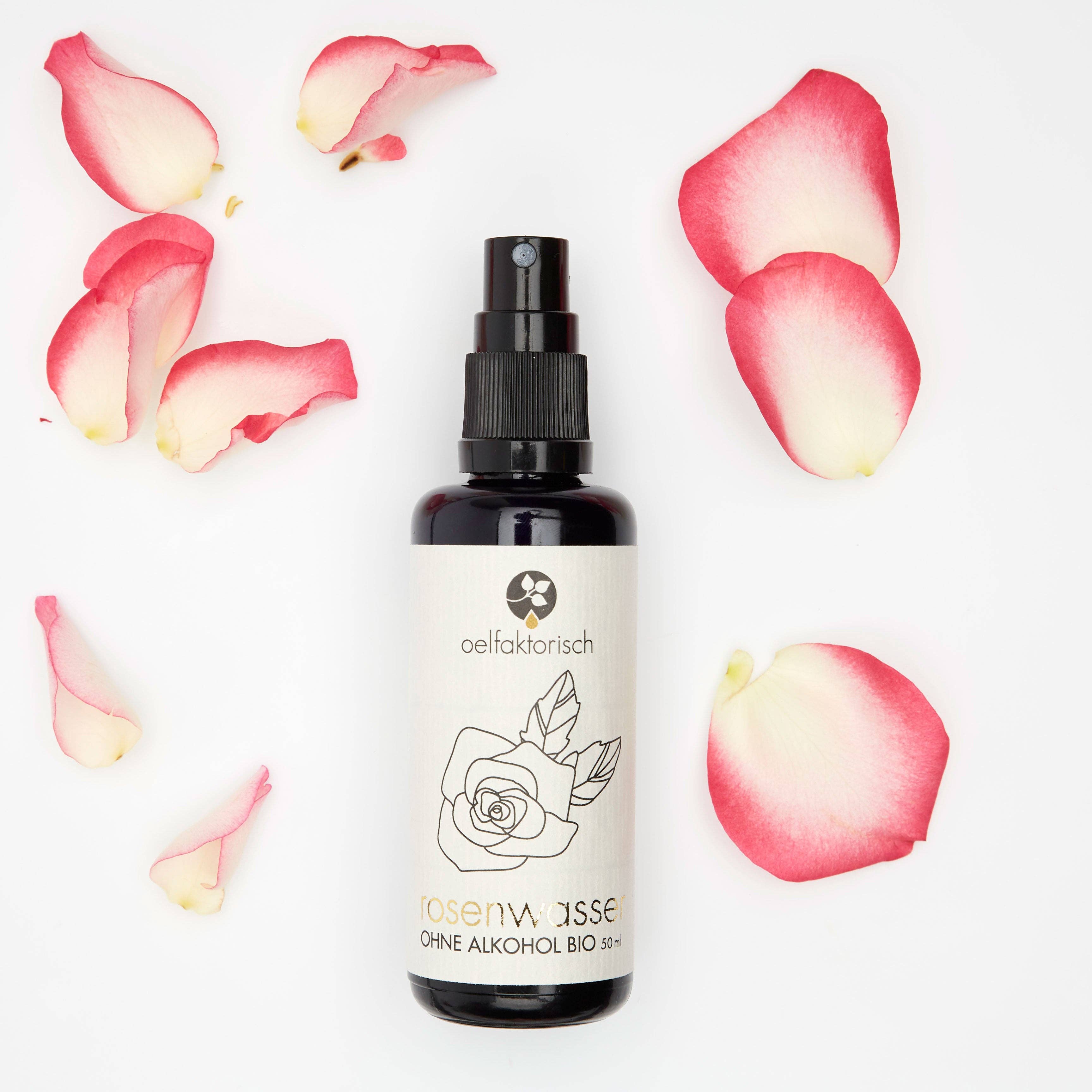 Flat lay of Damask Rosewater spray bottle surrounded by pink rose petals on a white background