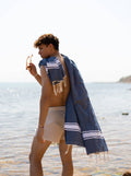 Ipanema Navy & White Fouta Towel 1x2m - lifestyle - Man standing by the sea with the towel draped over his shoulder.