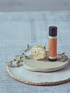 Dublin Herbalists Sweet Orange Lip Balm 5g - tube standing on a ceramic dish with a white rose